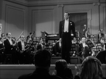 Movie still from “Unfaithfully Yours” (1948), directed by Preston Sturges – A man standing on a stage in front of an orchestra; Extreme Wide shot, Low angle