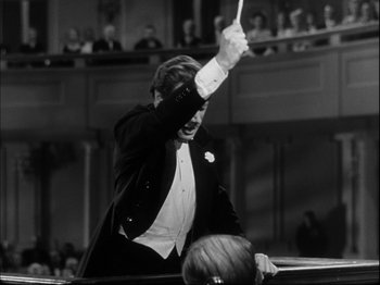 Movie still from “Unfaithfully Yours” (1948), directed by Preston Sturges – A man in a tuxedo is holding his hand up in the air; Medium shot, Low angle