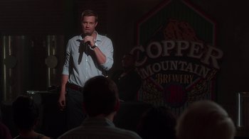 Movie still from “Unforgettable” (2017), directed by Denise Di Novi – A man standing in front of a microphone in front of a crowd; Wide shot, Over the shoulder angle