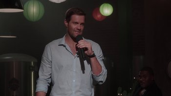 Movie still from “Unforgettable” (2017), directed by Denise Di Novi – A man holding a microphone while standing in front of a crowd; Medium shot, Over the shoulder angle