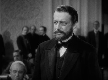 Movie still from “Union Pacific” (1939), directed by Cecil B. DeMille – A man in a suit and tie standing in front of a group of people; Close Up shot, Over the shoulder angle
