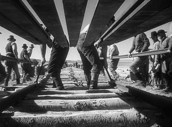 Movie still from “Union Pacific” (1939), directed by Cecil B. DeMille – A black and white photo of a group of people standing on a train track; Wide shot, Low angle