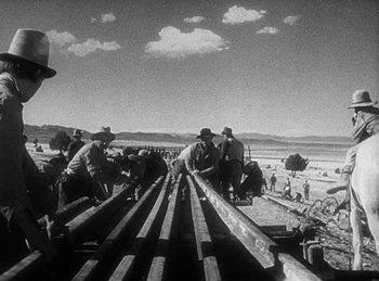 Movie still from “Union Pacific” (1939), directed by Cecil B. DeMille – A black and white photo of a group of men working on a train track; Wide shot, Low angle