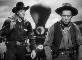 Movie still from “Union Pacific” (1939), directed by Cecil B. DeMille – Two men in cowboy hats standing in front of a train; Medium shot, Low angle