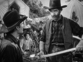 Movie still from “Union Pacific” (1939), directed by Cecil B. DeMille – A man in a cowboy hat holding a baseball bat in front of another man; Medium shot, Over the shoulder angle