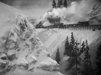Movie still from “Union Pacific” (1939), directed by Cecil B. DeMille – A train traveling on tracks through a snow covered forest; Extreme Wide shot, High angle