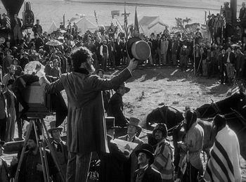 Movie still from “Union Pacific” (1939), directed by Cecil B. DeMille – A man holding a hat in front of a crowd of people; Wide shot, High angle