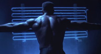 Movie still from “Universal Soldier: The Return” (1999), directed by Mic Rodgers – A man with his arms outstretched standing in front of a wall; Medium shot, Low angle