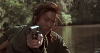 Movie still from “Universal Soldier: The Return” (1999), directed by Mic Rodgers – A woman holding a gun in front of a body of water; Medium shot, Low angle