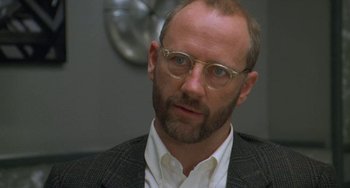 Movie still from “Universal Soldier: The Return” (1999), directed by Mic Rodgers – A person wearing glasses and a suit; Close Up shot, Over the shoulder angle