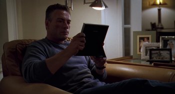 Movie still from “Universal Soldier: The Return” (1999), directed by Mic Rodgers – A man sitting on a couch looking at an ipad; Medium shot, Low angle