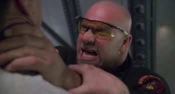 Movie still from “Universal Soldier: The Return” (1999), directed by Mic Rodgers – A bald man wearing glasses and a black shirt; Close Up shot, Low angle