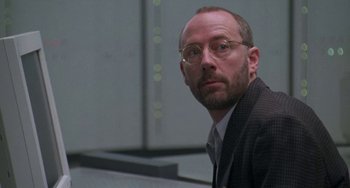 Movie still from “Universal Soldier: The Return” (1999), directed by Mic Rodgers – A man in a suit and tie wearing glasses; Close Up shot, Low angle