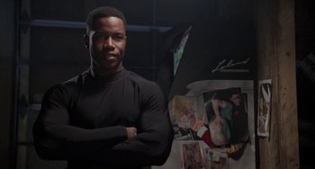 Movie still from “Universal Soldier: The Return” (1999), directed by Mic Rodgers – A man standing in front of a wall of pictures; Medium shot, Low angle