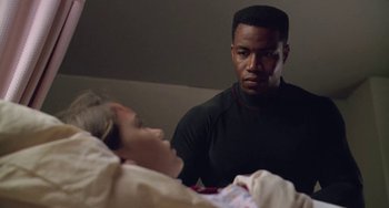 Movie still from “Universal Soldier: The Return” (1999), directed by Mic Rodgers – A man sitting in front of a woman in a bed; Medium shot, Over the shoulder angle