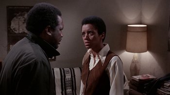 Movie still from “Uptight” (1968), directed by Jules Dassin – A man and a woman standing next to each other in front of a couch; Medium shot, Over the shoulder angle