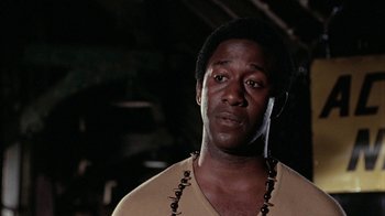 Movie still from “Uptight” (1968), directed by Jules Dassin – A man with a beard and a necklace is standing in a dark room; Close Up shot, Low angle