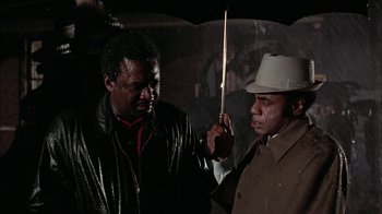 Movie still from “Uptight” (1968), directed by Jules Dassin – A man holding an umbrella over another man's head; Medium shot, Low angle