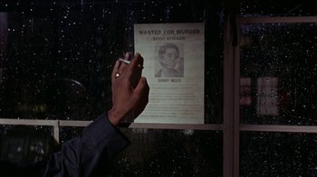Movie still from “Uptight” (1968), directed by Jules Dassin – A person holding a cigarette in front of a wanted poster; Close Up shot, High angle