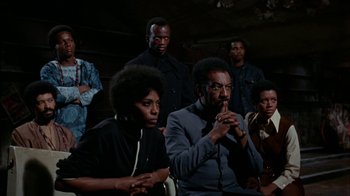 Movie still from “Uptight” (1968), directed by Jules Dassin – A group of men and women sitting in a room together; Medium shot, Low angle