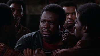 Movie still from “Uptight” (1968), directed by Jules Dassin – A group of men standing next to each other in a dark room; Close Up shot, Over the shoulder angle