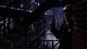 Movie still from “Uptight” (1968), directed by Jules Dassin – A man holding a gun while standing in front of stairs; Medium shot, Low angle