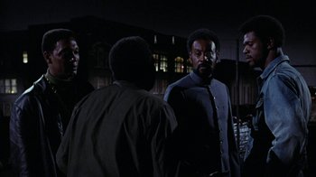 Movie still from “Uptight” (1968), directed by Jules Dassin – A group of men standing next to each other in the dark; Medium shot, Over the shoulder angle