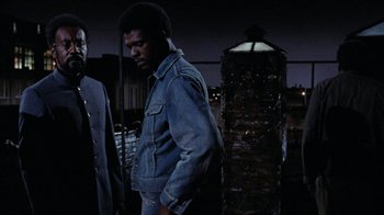 Movie still from “Uptight” (1968), directed by Jules Dassin – A man in a jean jacket standing next to another man; Medium shot, Low angle