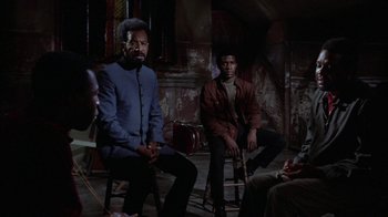Movie still from “Uptight” (1968), directed by Jules Dassin – A group of men sitting on chairs in a darkened room; Medium shot, High angle
