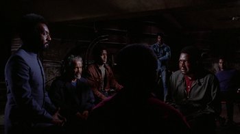 Movie still from “Uptight” (1968), directed by Jules Dassin – A group of men sitting in a dark room; Medium shot, Over the shoulder angle