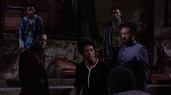 Movie still from “Uptight” (1968), directed by Jules Dassin – A group of people standing around in a room; Medium shot, Low angle