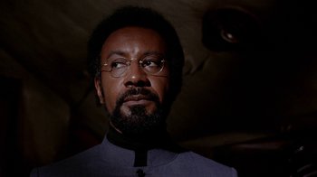 Movie still from “Uptight” (1968), directed by Jules Dassin – A person wearing glasses and a suit; Close Up shot, Low angle