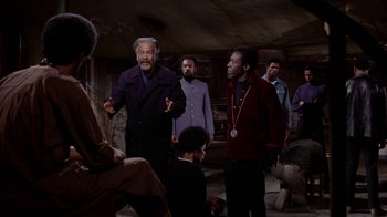 Movie still from “Uptight” (1968), directed by Jules Dassin – A group of men standing around in a room; Medium shot, Over the shoulder angle