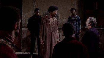 Movie still from “Uptight” (1968), directed by Jules Dassin – A group of men standing next to each other in a room; Medium shot, Over the shoulder angle