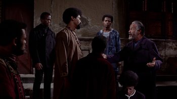 Movie still from “Uptight” (1968), directed by Jules Dassin – A group of men standing around each other in front of a wall; Medium shot, Over the shoulder angle