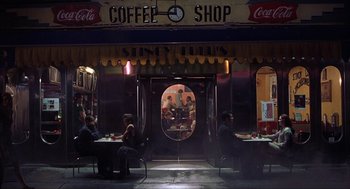 People sitting at tables in front of a coffee shop at night