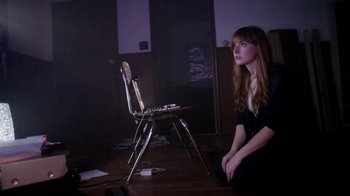 Movie still from “V/H/S/2” (2013), directed by Timo Tjahjanto – A woman sitting in front of a chair in a dark room; Medium shot, Low angle