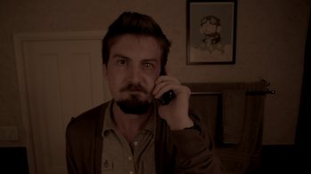 Movie still from “V/H/S/2” (2013), directed by Timo Tjahjanto – A man is talking on a cell phone in a room; Medium shot, High angle
