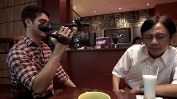 Movie still from “V/H/S/2” (2013), directed by Timo Tjahjanto – A man holding a video camera up to his face; Medium shot, Over the shoulder angle
