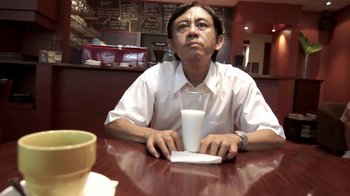 Movie still from “V/H/S/2” (2013), directed by Timo Tjahjanto – A man sitting at a table with a drink in front of him; Close Up shot, Over the shoulder angle