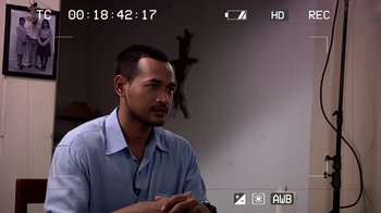 Movie still from “V/H/S/2” (2013), directed by Timo Tjahjanto – A man sitting in front of a cross on a wall; Close Up shot, Over the shoulder angle