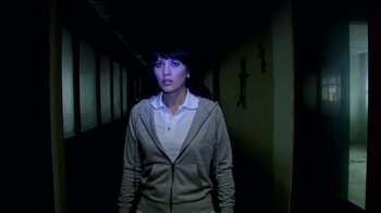 Movie still from “V/H/S/2” (2013), directed by Timo Tjahjanto – A woman standing in a dark hallway looking at the camera; Medium shot, Low angle
