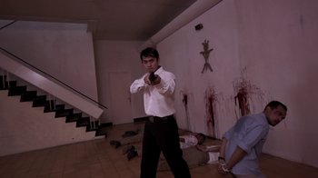 Movie still from “V/H/S/2” (2013), directed by Timo Tjahjanto – A man holding a gun in a room with blood on the floor; Wide shot, Low angle