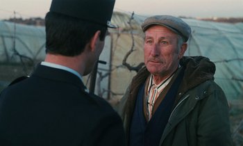 Movie still from “Vagabond” (1985), directed by Agnès Varda – An older man wearing a hat talking to another man; Close Up shot, Over the shoulder angle