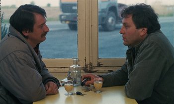 Movie still from “Vagabond” (1985), directed by Agnès Varda – Two men sitting at a table in front of a window; Close Up shot, High angle