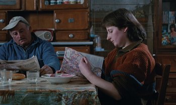 Movie still from “Vagabond” (1985), directed by Agnès Varda – A woman sitting at a table with a bowl of food; Medium shot, Over the shoulder angle