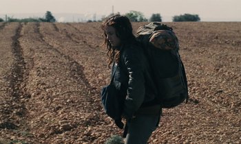 Movie still from “Vagabond” (1985), directed by Agnès Varda – A woman walking across a field with a backpack; Wide shot, High angle
