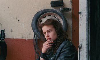Movie still from “Vagabond” (1985), directed by Agnès Varda – A young woman with long brown hair is leaning up against a wall; Close Up shot, High angle
