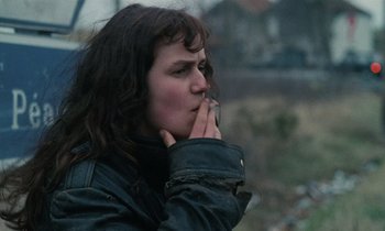 Movie still from “Vagabond” (1985), directed by Agnès Varda – A woman is smoking a cigarette outside on a cold day; Close Up shot, Low angle