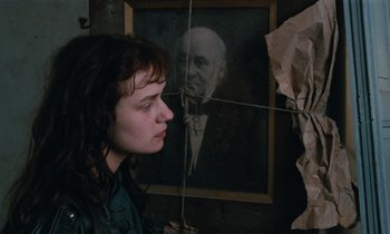 Movie still from “Vagabond” (1985), directed by Agnès Varda – A woman standing in front of a painting of an old man; Close Up shot, Over the shoulder angle